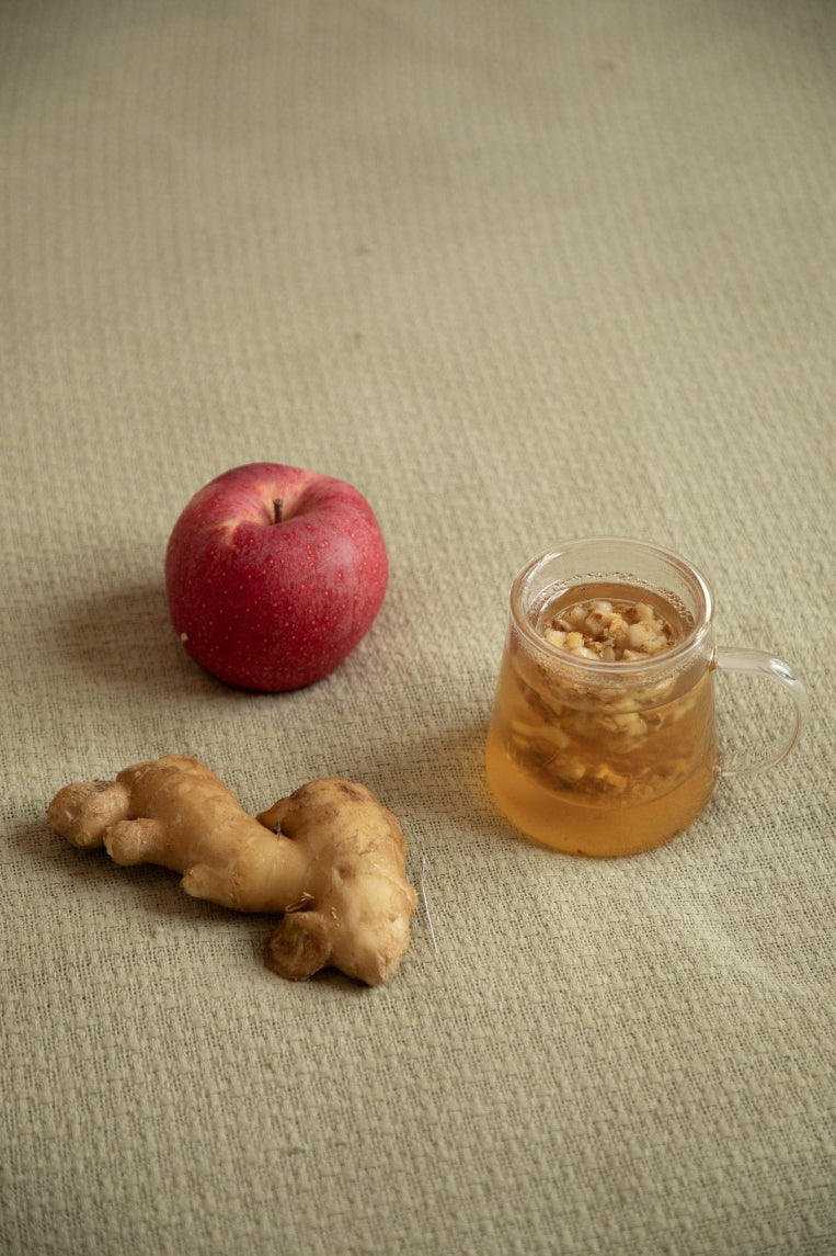 Glass mug with ginger tea, fresh ginger root, and an apple on a textured surface