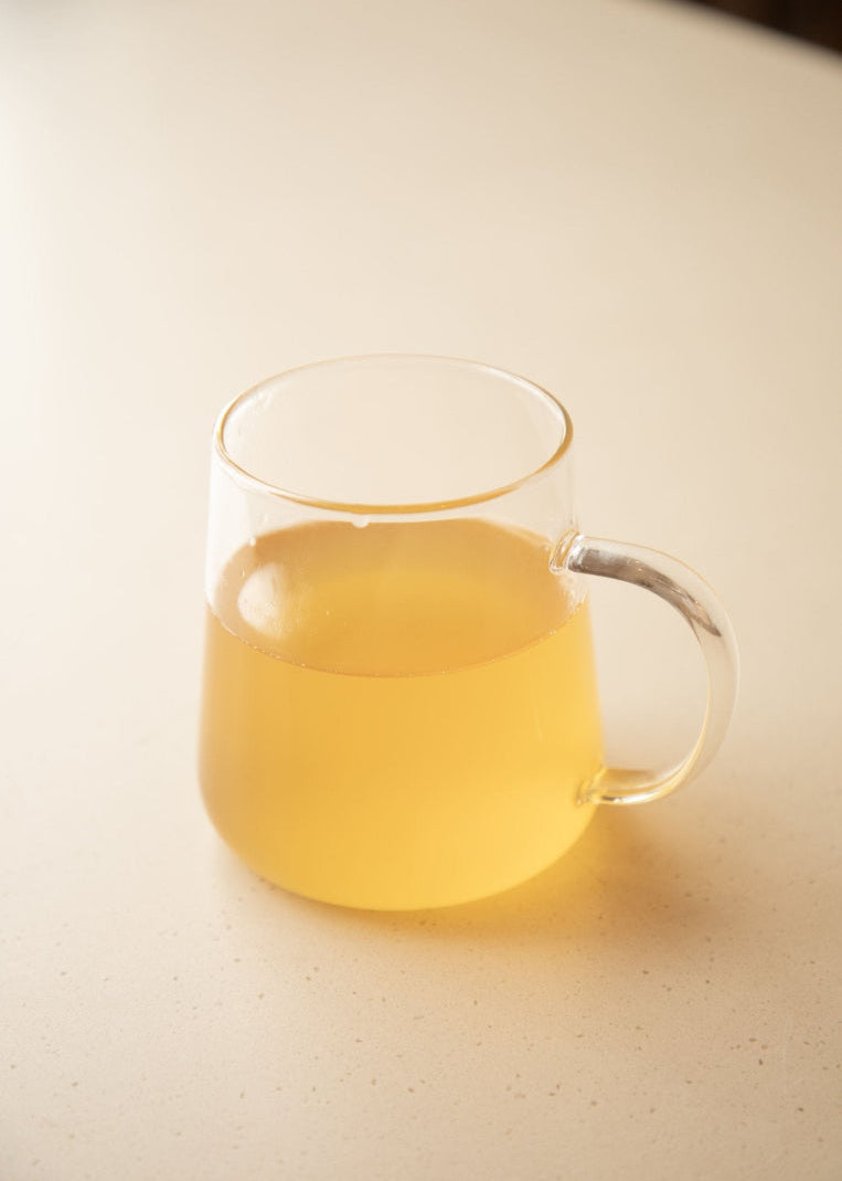 Clear glass mug with yellow liquid on a light surface