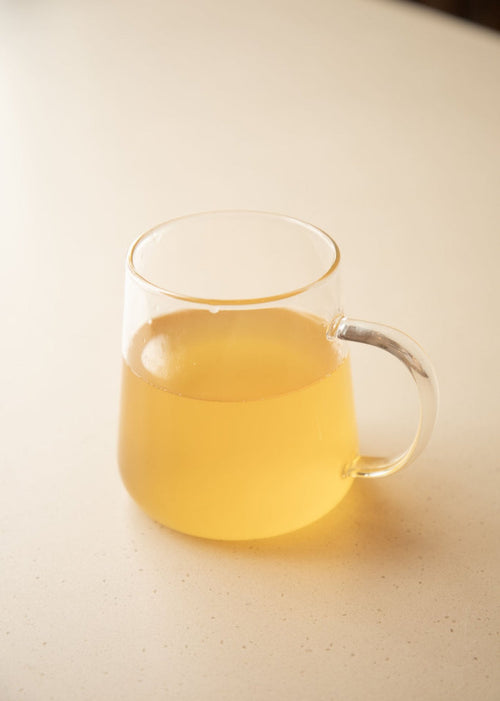 Clear glass mug with yellow liquid on a light surface