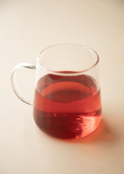 Clear glass mug filled with red liquid on a light beige background
