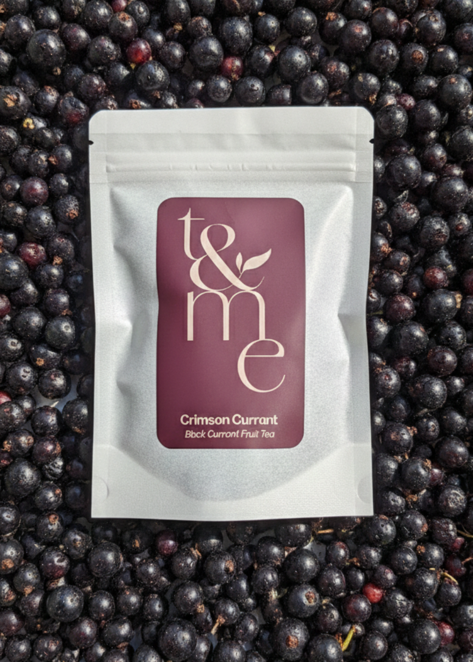 Tea package labeled 't&me' on a bed of black currants